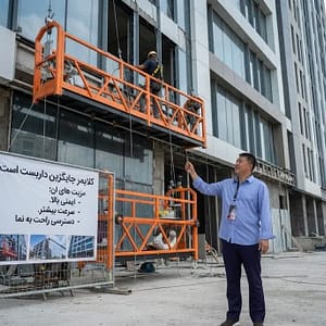 تصوصیری از یک کلایمر ساختمانی در حال کار بر روی نمای ساختمان است. همراه با بنر فارسی مزایای کلایمر